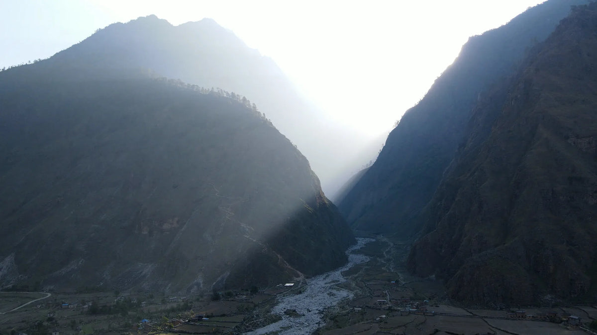 Sunlight flooding a deep Himalayan valley with a river and terraced village far below