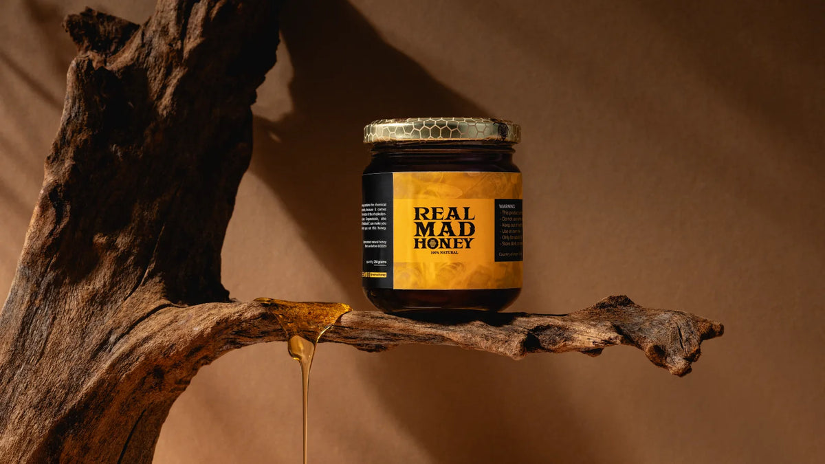 A jar of Real Mad Honey resting on driftwood with honey dripping down, in warm evening light