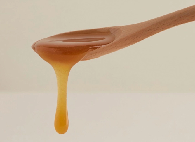 Thick dark amber honey running off a wooden teaspoon