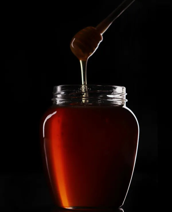 Honey dripping from a dipper into a glass jar