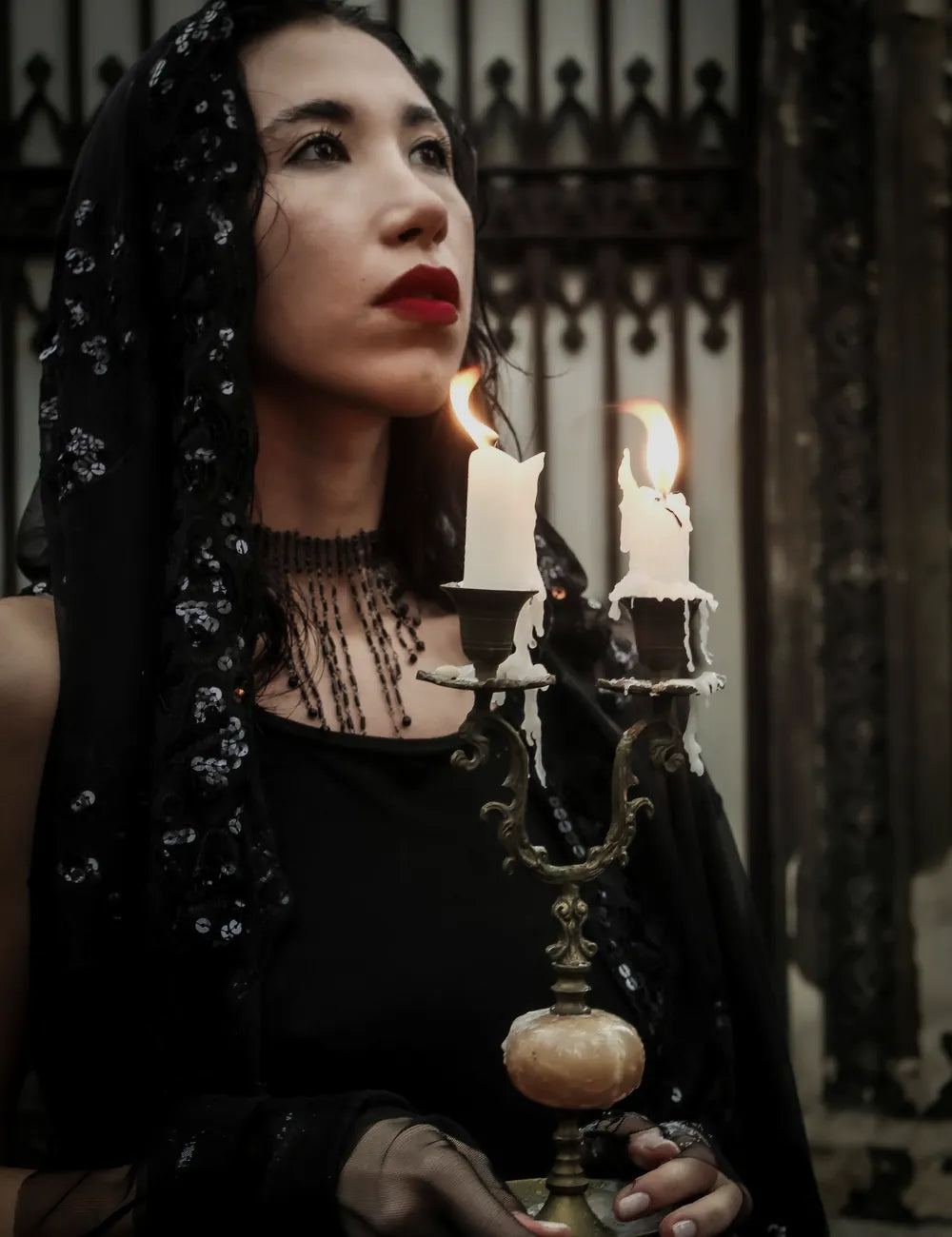 Gothic woman holding a candelabra at a dark iron gate